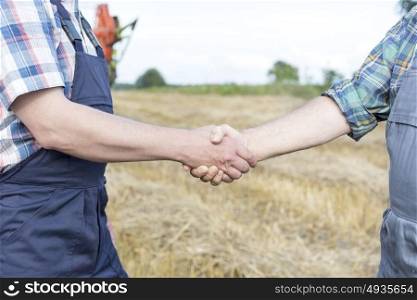 Midsection of farmers shaking hands while standing on field at farm