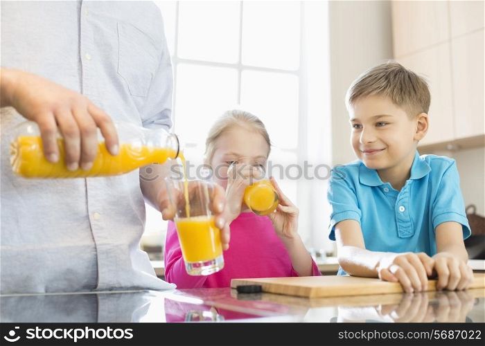 Midsection of father serving orange juice for children in kitchen