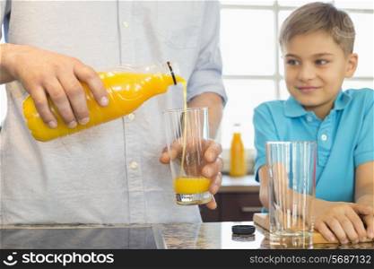 Midsection of father serving orange juice for son in kitchen