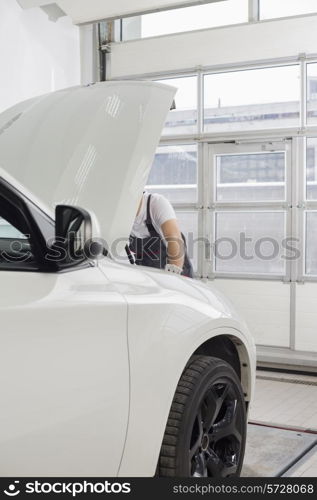 Midsection of male automobile mechanic examining car engine in workshop