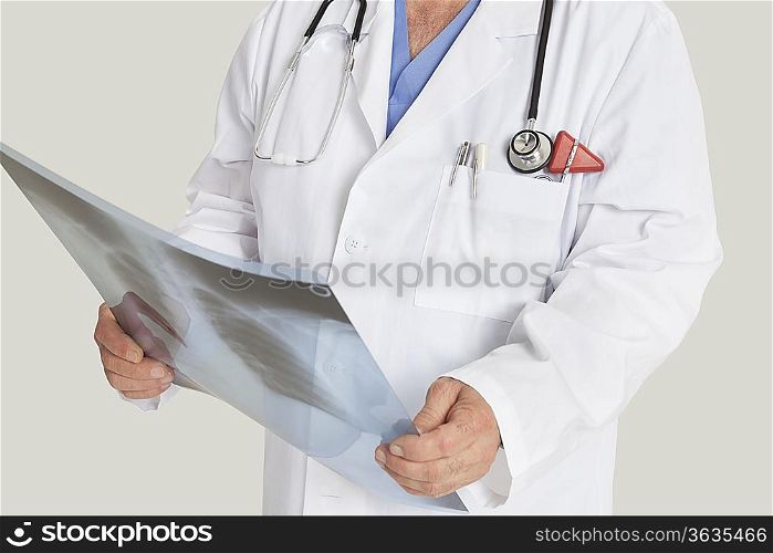 Midsection of male doctor with x-ray report over gray background