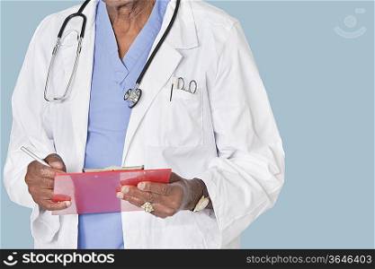 Midsection of male doctor writing on clipboard over light blue background