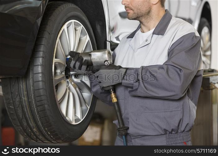 Midsection of male mechanic repairing car&rsquo;s wheel in workshop