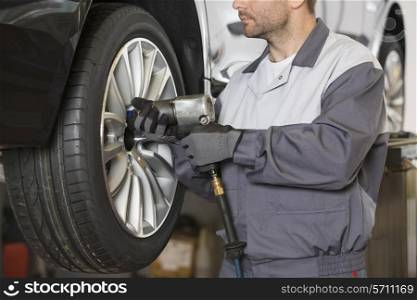Midsection of male mechanic repairing car&rsquo;s wheel in workshop
