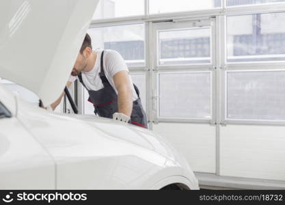 Midsection of male technician repairing car engine in workshop