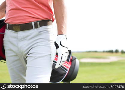 Midsection of man carrying golf club bag while walking at course