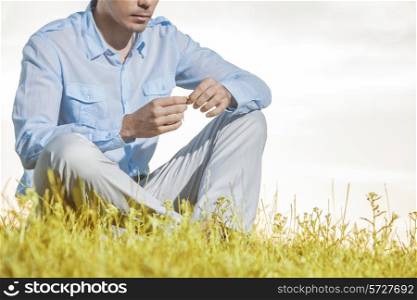Midsection of man holding flower while sitting on grass against clear sky