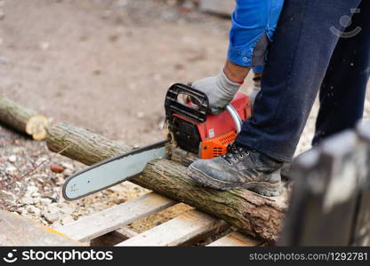 Midsection of man holding the chainsaw cutting wood timber trunk in autumn or winter day in the yard outdoor