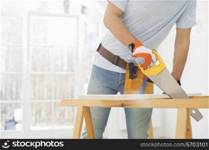 Midsection of man sawing wood in new house