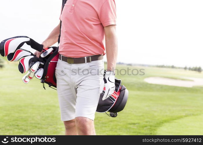 Midsection of man with golf club bag standing at course