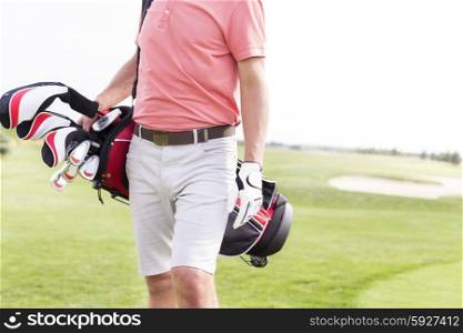 Midsection of man with golf club bag standing at course