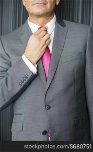 Midsection of mature businessman adjusting necktie
