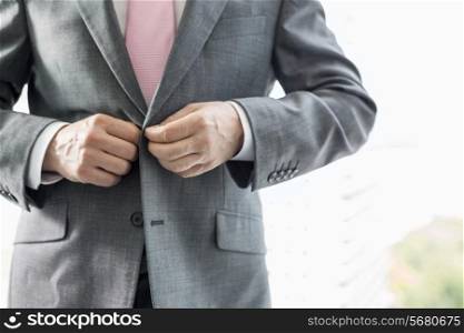 Midsection of mature businessman buttoning his blazer