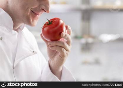 Midsection of mature chef smelling fresh red tomato while standing at restaurant kitchen