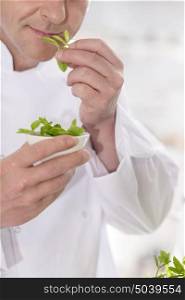 Midsection of mature chef smelling herb leaves in kitchen at restaurant