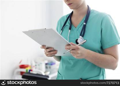 Midsection of nurse with medical documents on clipboard at hospital