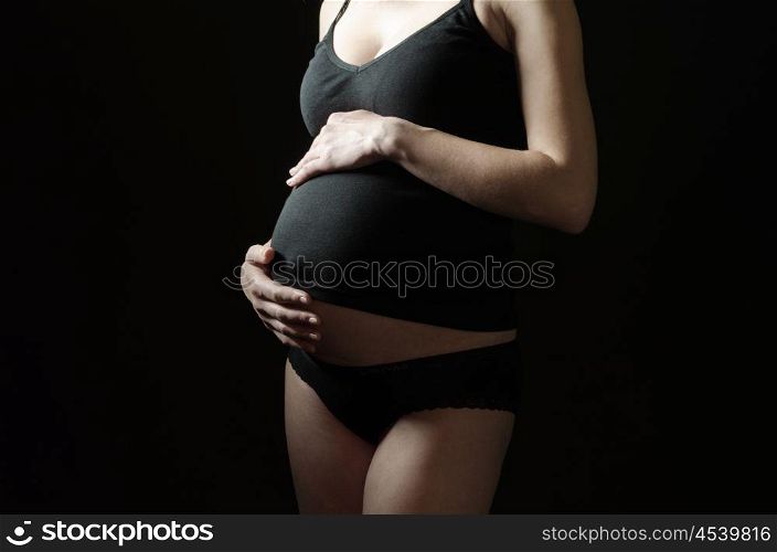 midsection of pregnant woman in black clothes on a black background