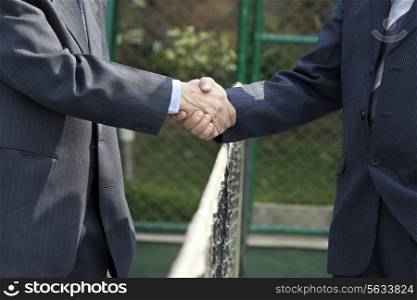 Midsection of professionals shaking hands over tennis net in court