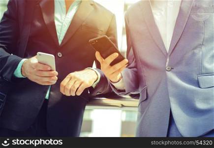 Midsection of two colleague businessmen using smartphone at the outside of modern office building, business and technology concept