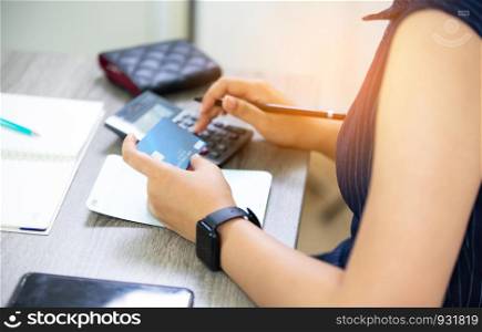 midsection of woman with credit card book bank and calculator paying bills online indoor
