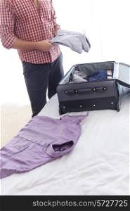 Midsection of young businessman unpacking luggage in hotel room