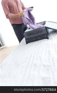 Midsection of young businessman unpacking suitcase in hotel room