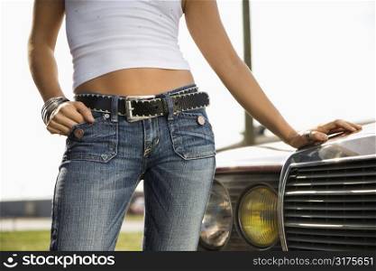 Midsection of young Caucasian woman standing beside automobile.