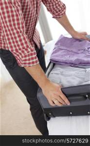 Midsection of young man unpacking suitcase in hotel room
