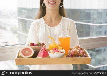 midsection woman holding wooden tray with many fruits juice
