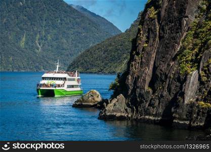 "MILFORD SOUND, NEW ZEALAND - DECEMBER 8, 2016: Tour boat cruises out into Milford Sound in Fiordland National Park. Milford Sound was described as "the eight wonder of the world" by Rudyard Kipling."