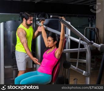 Military press machine woman with personal trainer workout at gym