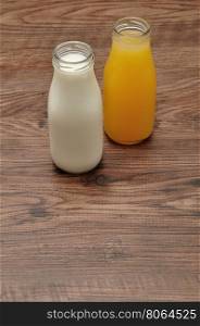 Milk and orange juice in bottles isolated against a wooden background