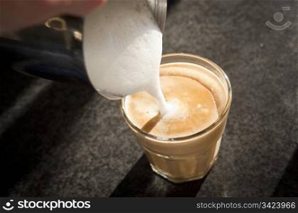 Milk being poured into a modern latte glass from above