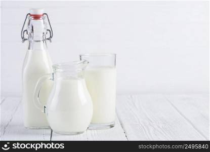 Milk bottle with jug and glass of milk on vintage white wooden table