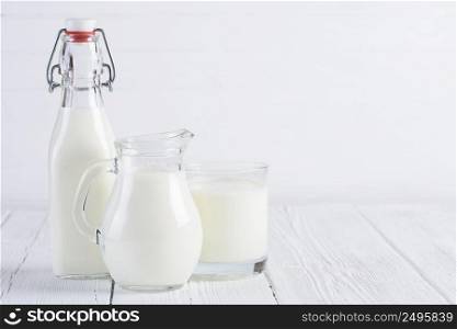 Milk bottle with jug and glass of milk on white wooden table