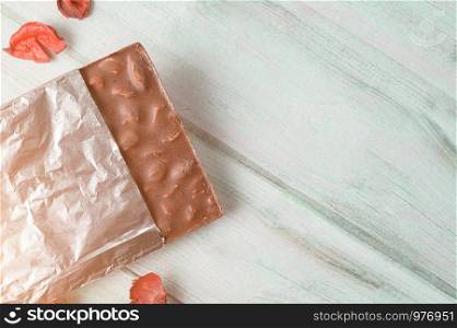 Milk chocolate bar with almonds wrapped in aluminium foil on wooden table. Copy space wallpaper.