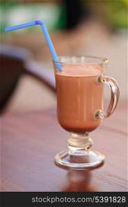 Milk chocolate beverage with straw in glass on table