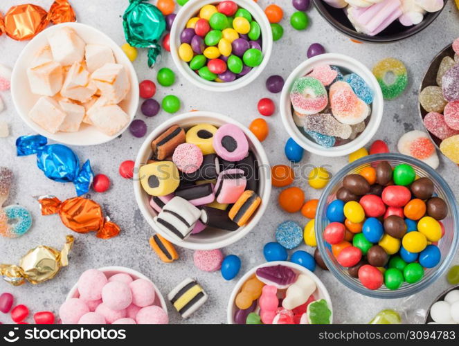 Milk chocolate candies woth shell in jar with various jelly gums candies on white table with liquorice allsorts and strawberry bonbons with different sour sugar gums.