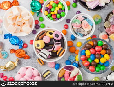 Milk chocolate candies woth shell in jar with various jelly gums candies on white table with liquorice allsorts and strawberry bonbons with different sour sugar gums.