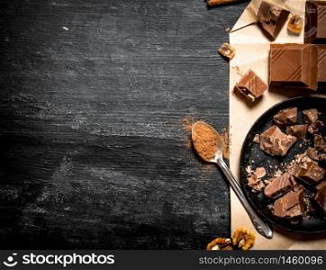 Milk chocolate with cocoa. On a black wooden background.. Milk chocolate with cocoa.
