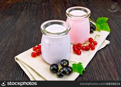 Milk cocktail with black and red currants in glass jars on a napkin with berries on a dark wooden board background