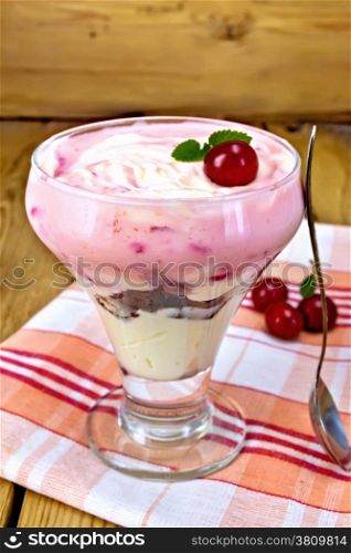 Milk dessert with cherry, chocolate biscuit and curd, a spoon, a linen napkin, cherries on a background of wooden boards