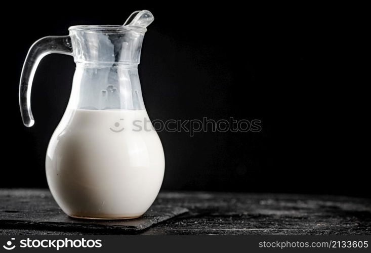 Milk in a jug on the table. On a black background. High quality photo. Milk in a jug on the table.