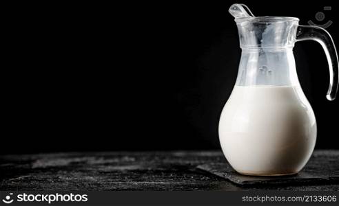 Milk in a jug on the table. On a black background. High quality photo. Milk in a jug on the table.
