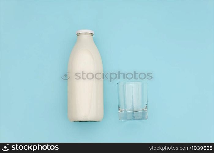 Milk in glass bottle and empty glass on blue background with copy space. Flat lay top view.. Milk in glass bottle and empty glass on blue background with copy space. Flat lay top view