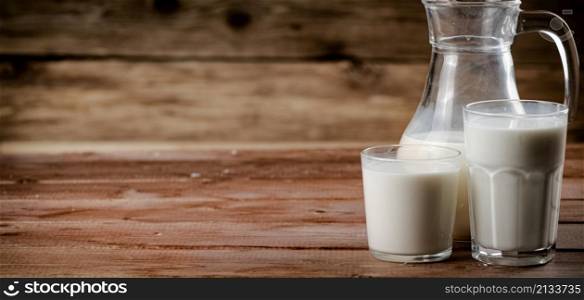 Milk in jugs and glasses. On a wooden background. High quality photo. Milk in jugs and glasses.