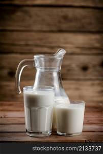 Milk in jugs and glasses. On a wooden background. High quality photo. Milk in jugs and glasses.