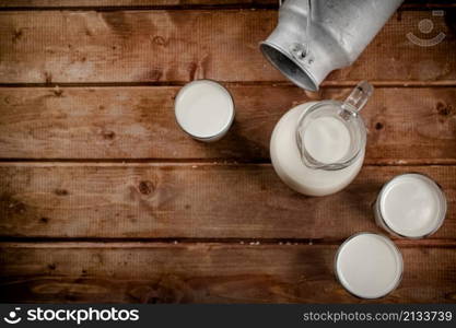 Milk in jugs and glasses. On a wooden background. High quality photo. Milk in jugs and glasses.