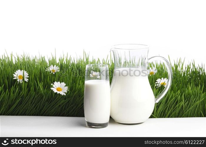 Milk jug and glass on fresh green grass with chamomiles isolated on white