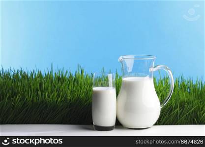 Milk jug and glass on grass field. Milk jug and glass on fresh green grass field background